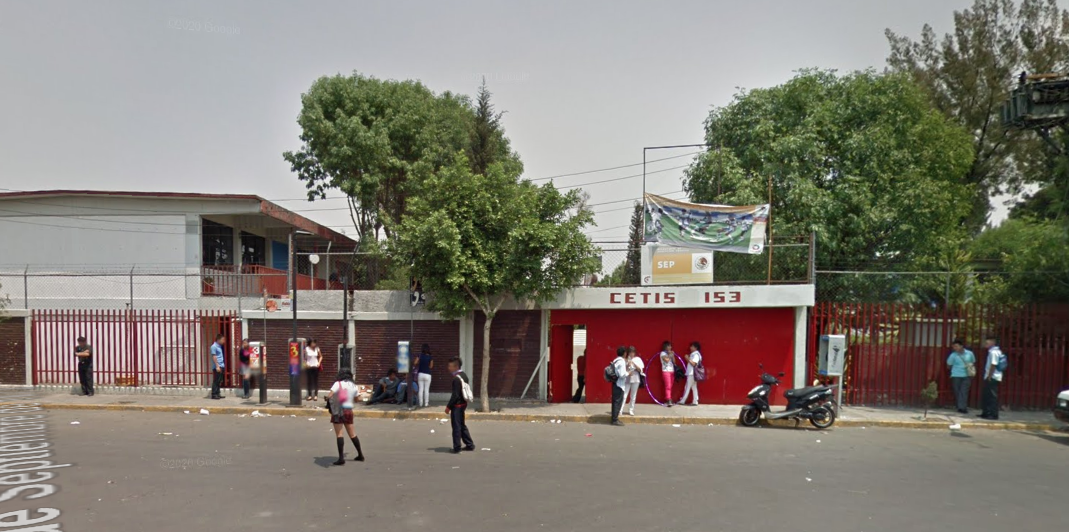 Fotografía en la que se muestra la fachada del plantel, conformada por muros de ladrillo intercalados con rejas de color rojo. A la mitad de las rejas y los muros se encuentra un portón de color rojo por el cual se puede ingresar a las instalaciones. Arriba del portón, en letras grandes, dice CETIS 153.
